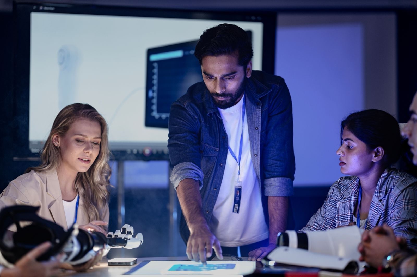A team of diverse engineers collaborating over technical diagrams and robotics hardware in a modern development lab.
