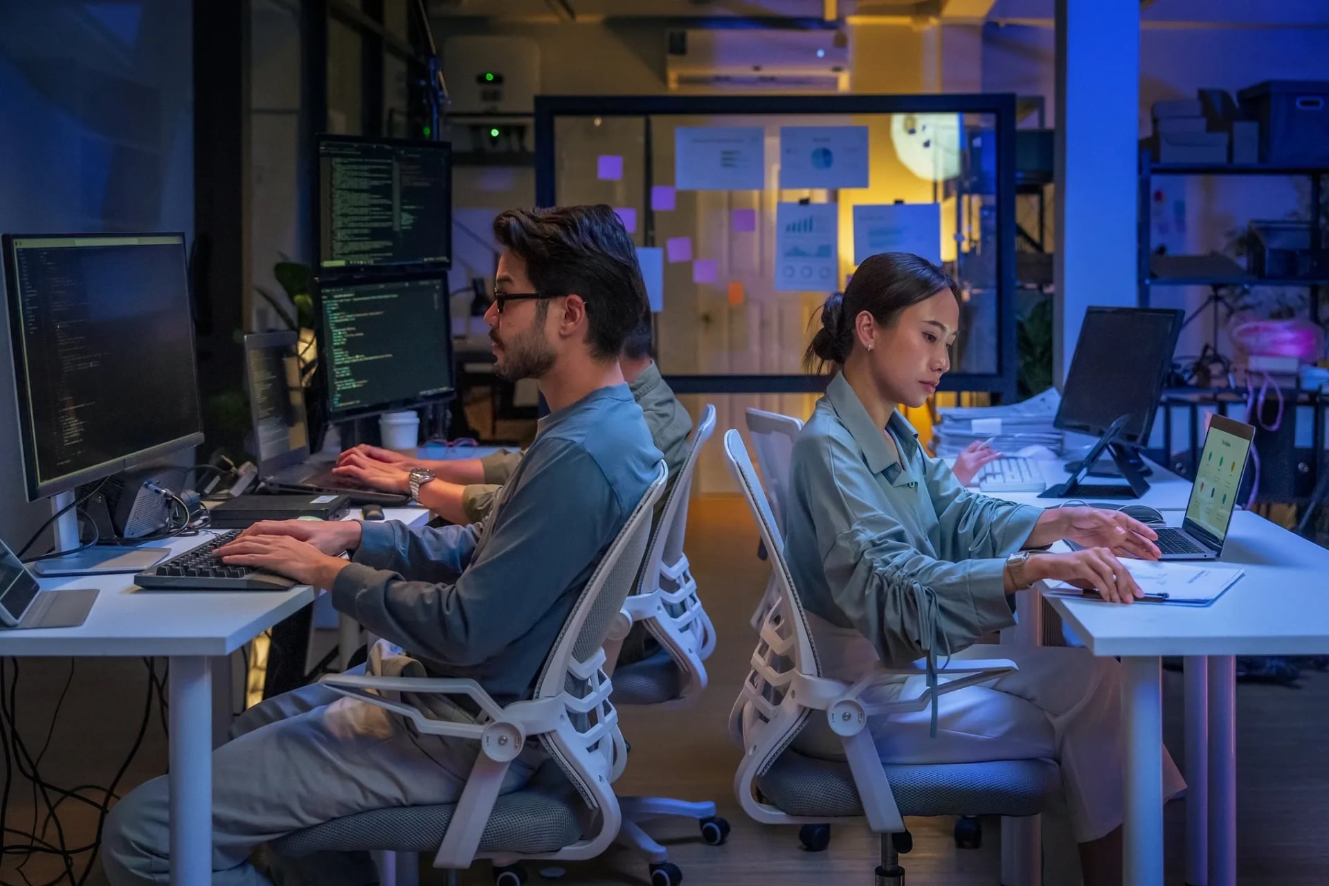 Two software engineers working focused at their computer stations in a modern, low-lit office, representing a dedicated and experienced AI development team.